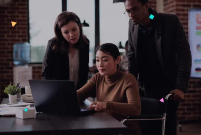 Three professionals collaborating around a laptop in an office setting.