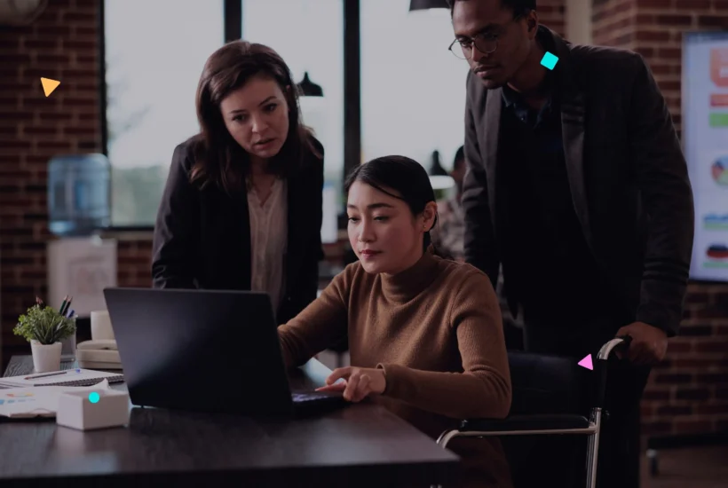 Three professionals collaborating around a laptop in an office setting.