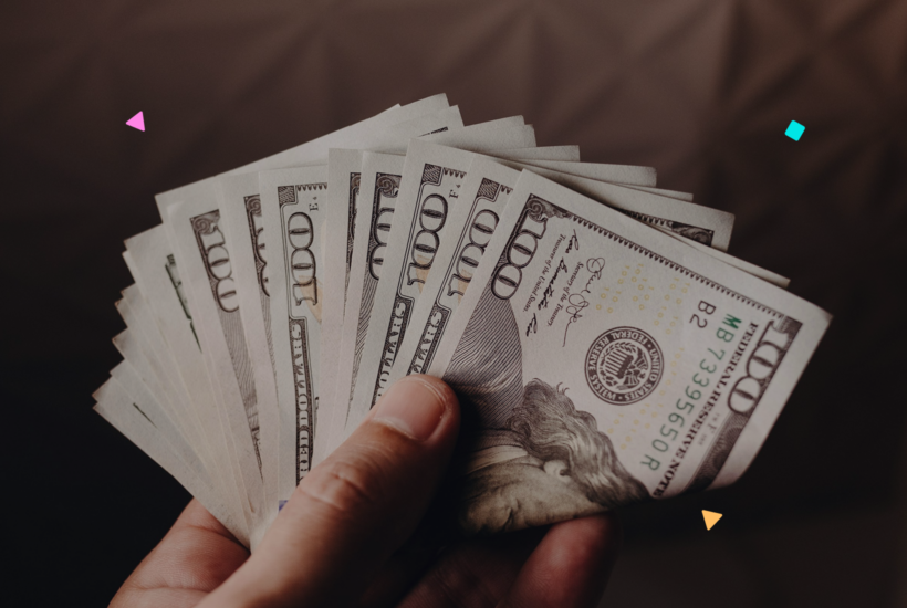 Hand holding 100-dollar bills, representing recurring revenue from WordPress maintenance plans.